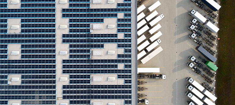 aerial photo of an industrial facility with solar panels on roof and semi trucks in parking lot